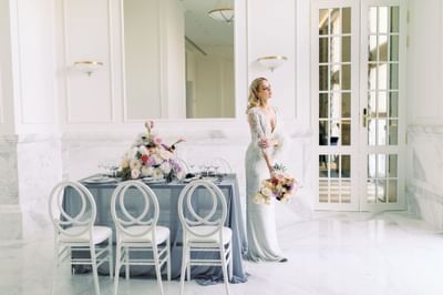 Bride holding flowers and standing by dining setup in a room at Polonia Palace Hotel