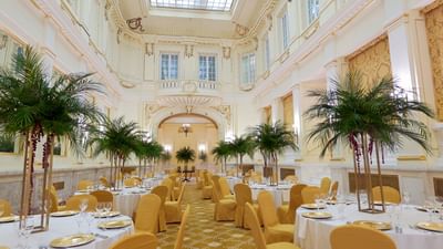 Banquet hall with dining tables, grand decor, and palm trees at Polonia Palace Hotel