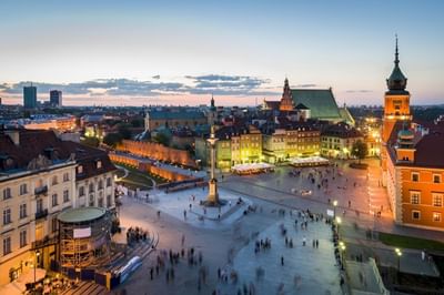 Aerial view of bustling Warsaw square at twilight with illuminated buildings near Polonia Palace Hotel