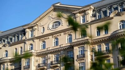 The facade of Polonia Palace Hotel with classic architecture framed by blurred leaves
